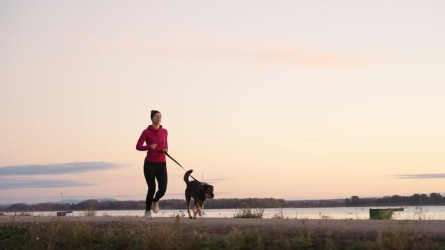 A woman is jogging alongside her dog during the breathtaking sunrise by the water