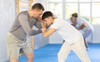 Obraz premium Two men at group judo lesson practicing techniques in sparring, in background men are practicing techniques too