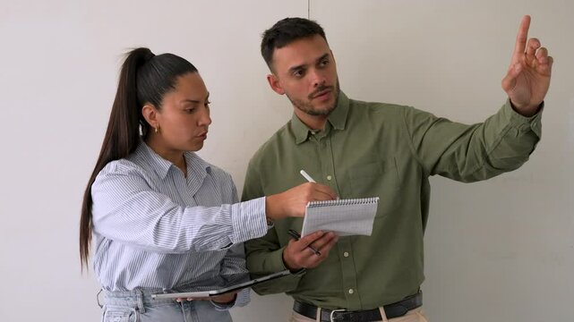 Two business colleagues are discussing strategy, with a woman taking notes on a tablet and a man pointing and explaining something