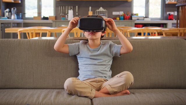 Boy Sitting On Sofa At Home Wearing Virtual Reality Headset - Powered by Adobe