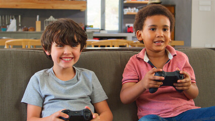 Two Young Boys Sitting On Sofa At Home Playing Computer Game Together