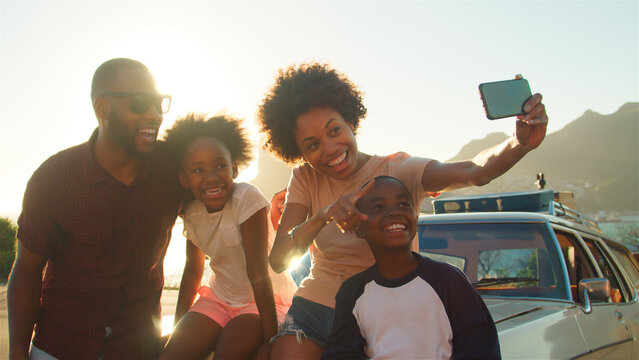 Family Posing For Selfie Next To Car Packed For Road Trip