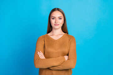 Portrait of a confident young woman in a stylish brown sweater against a bright blue background,...