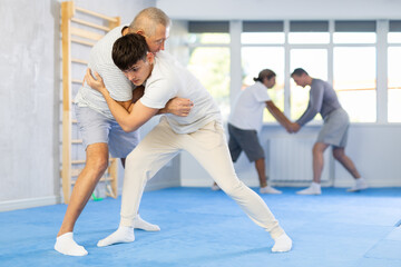 Obraz premium Guy and senior man athletes practice Brazilian jiu Jitsu Aikido Wing chun wrestling. Training at Academy of Martial Arts martial arts hand-to-hand combat.