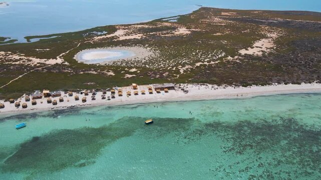 The beach is lined with several yellow umbrellas for shade, and the water appears to be crystal blue.
