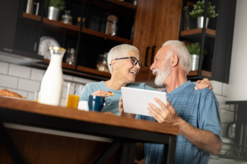 Happy senior couple using digital tablet at breakfast in cozy kitchen