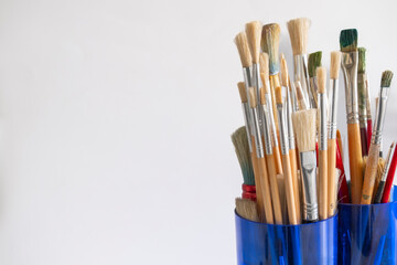 Fototapeta premium Oil paint brushes of various sizes in a blue glass container
