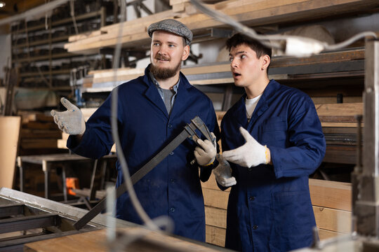 Two young male carpenters discussing work process in wood workshop
