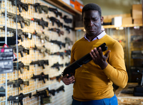 African american man chooses pump-action shotgun in gun store