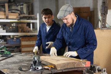 Young man worker measures wooden plank with tape measure in wood workshop