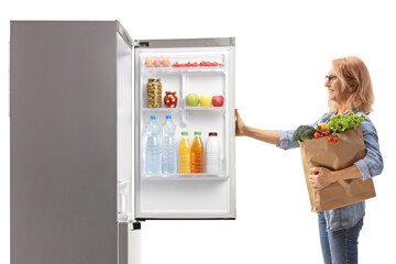 Woman with a grocery bag opening a fridge
