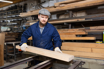 Young man worker in carpentry workshop putting wooden board on cutting machine