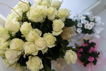 Elegant bouquet of white roses accompanied by small arrangements of daisies and pink roses on a light surface. Ideal for wedding, anniversary, or romantic occasions