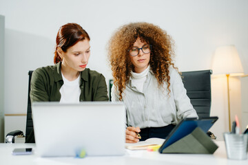 Two female professionals in smart casual outfits collaborate over finance charts and reports in a...