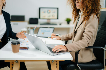Two female professionals in smart casual outfits collaborate over finance charts and reports in a...