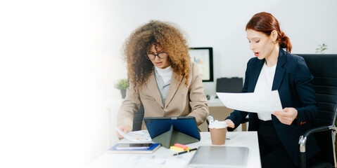 Two female professionals in smart casual outfits collaborate over finance charts and reports in a...