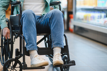 Customer using wheelchair pushing wheels in supermarket while shopping for groceries