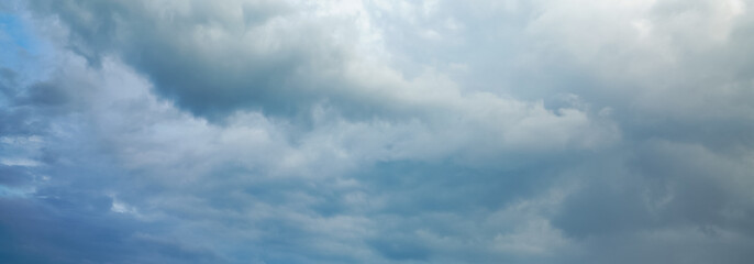 Dark storm clouds gather across the blue sky during the rainy season, forming dramatic shapes as...