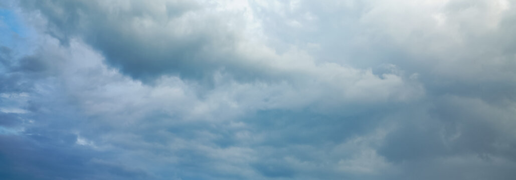 Dark storm clouds gather across the blue sky during the rainy season, forming dramatic shapes as nature signals an approaching storm over the open landscape.