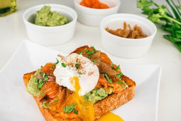  fresh breakfast plate with poached eggs, flowing yolk, smoked salmon guacamole on toast homemade healthy and served on bread.