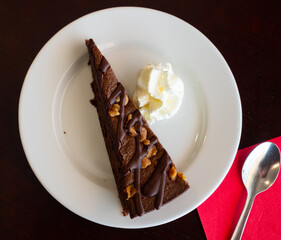 Sweet tender piece of chocolate-nut pie decorated with ball of cream ice cream is served on plate. Gastro tourism, acquaintance with culinary traditions of countries, gourmet restaurant