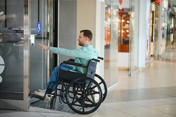 Customer in wheelchair calling the elevator in a modern shopping mall