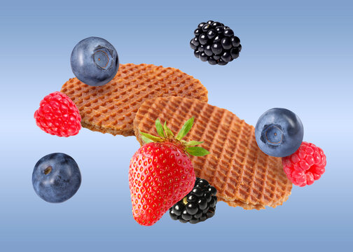 Tasty Dutch waffles and fresh berries flying on blue gradient background