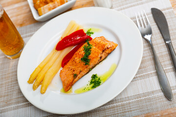 Porion of salmon fillet with white asparagus and red pepper served on table.