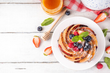 Sweet summer bundt cake with fresh fruit and berry. Traditional round sponge cake, seasonal dessert with strawberry, raspberry, blueberry, honey and sugar sprinkles, white wooden table copy space
