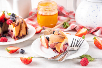 Sweet summer bundt cake with fresh fruit and berry. Traditional round sponge cake, seasonal dessert with strawberry, raspberry, blueberry, honey and sugar sprinkles, white wooden table copy space