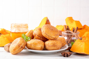 Autumn pumpkin pie donuts with cinnamon sugar sprinkled topping and pumpkin spice filling, on white wooden table with honey and pumpkin squash slices, copy space