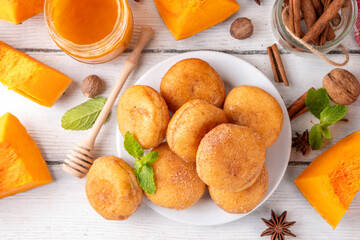 Autumn pumpkin pie donuts with cinnamon sugar sprinkled topping and pumpkin spice filling, on white wooden table with honey and pumpkin squash slices, copy space