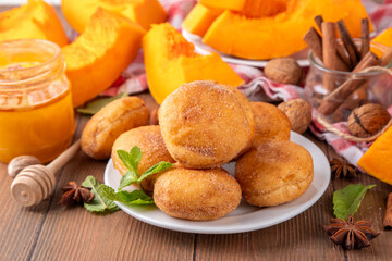 Autumn pumpkin pie donuts with cinnamon sugar sprinkled topping and pumpkin spice filling, on white wooden table with honey and pumpkin squash slices, copy space