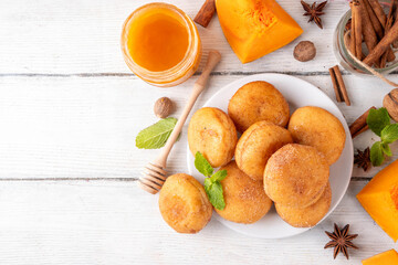 Autumn pumpkin pie donuts with cinnamon sugar sprinkled topping and pumpkin spice filling, on white wooden table with honey and pumpkin squash slices, copy space