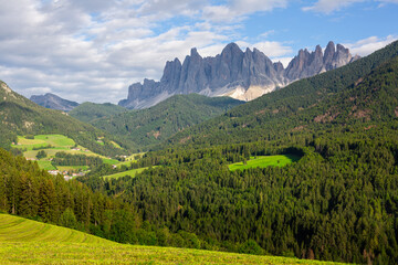 Fototapeta premium Picturesque landscapes of alpine highland valley of Val di Funes located at foot of rocky mountains of Italian Dolomites with green meadows, dense forests and charming rustic houses on sunny day