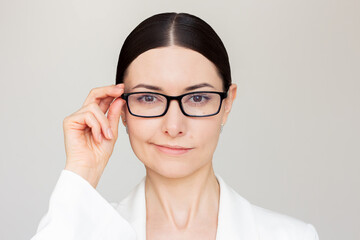 Young caucasian pretty brunette woman in white suit with glasses holding her glasses with hand and...
