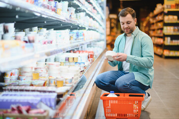 Customer choosing yogurt in dairy products section of supermarket