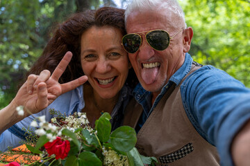 beautiful and harmonious middle-aged couple smiling and taking funny selfie making peace sign with hand outdoors