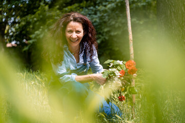 smiling middle-aged woman with red hair showing a bunch of flowers sitting in the grass