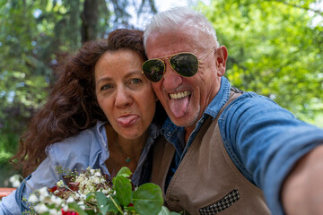 beautiful and harmonious middle-aged couple takes a funny selfie making faces outdoors