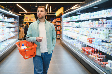 Customer carrying shopping basket walking in supermarket dairy aisle