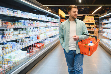 Customer walking through dairy products aisle holding shopping basket in supermarket