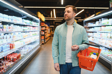 Customer choosing groceries walking in supermarket holding shopping basket