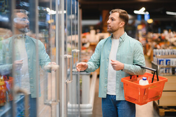 Customer opening refrigerator door in supermarket, choosing frozen food products