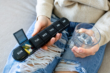 Close up of person holding pill organizer and glass of water on ripped jeans