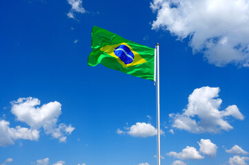 The flag of Brazil flutters in the wind in a blue sky with white clouds