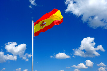 The flag of Spain flutters in the wind in a blue sky with white clouds
