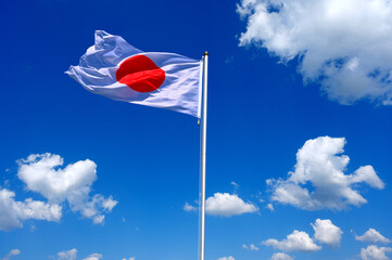 The flag of Japan flutters in the wind in a blue sky with white clouds