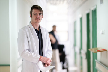 Fototapeta premium Doctor Reading Documents in Hospital.Young male doctor walking in hospital hallway while reading patient documentation. Clinical work environment.