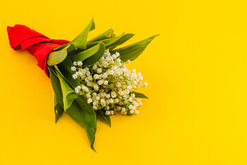 Bouquet of lily-of-the-valley with red ribbon on yellow backdrop